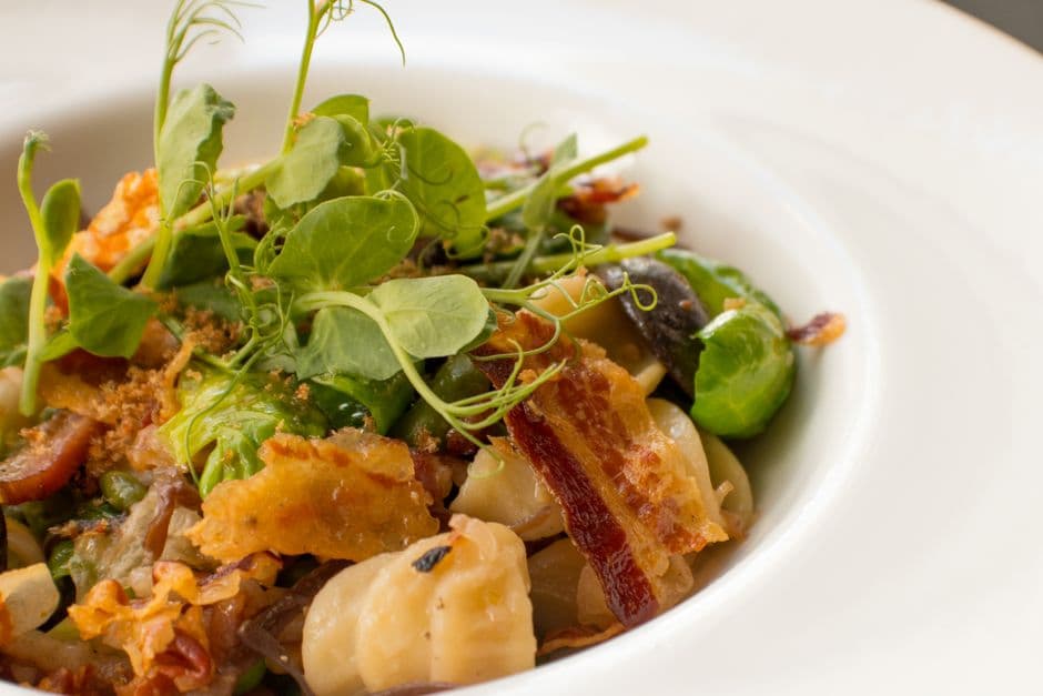 Plated pasta dish with brussels sprouts, crispy bacon, and pea shoots
